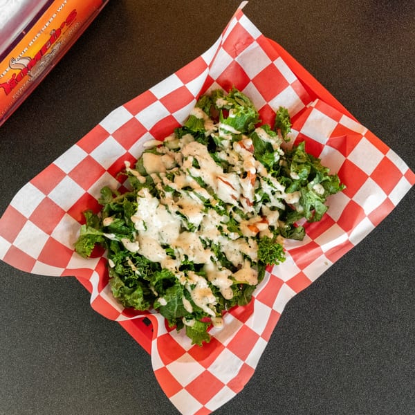 Romeo's Vegan Burgers side salad with green lettuce, tomatoes, and creamy dressing in a red checkered basket.