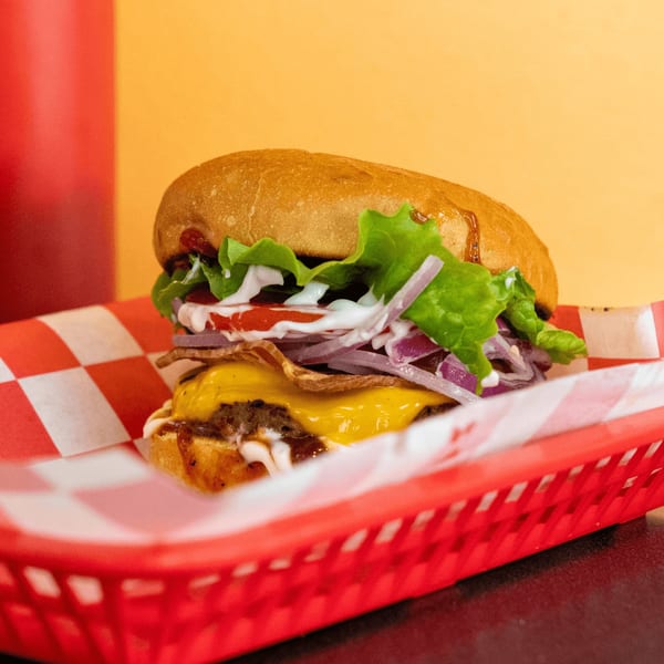 A Romeo's Vegan Burger with cheese, lettuce, tomato, onion, and sauce in a red basket.