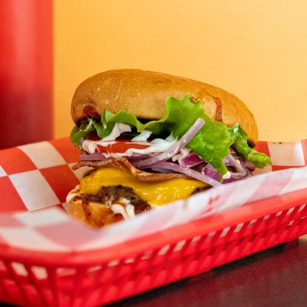 Romeo's Vegan Burger with lettuce, tomato, onion, cheese, and sauce in a red basket.