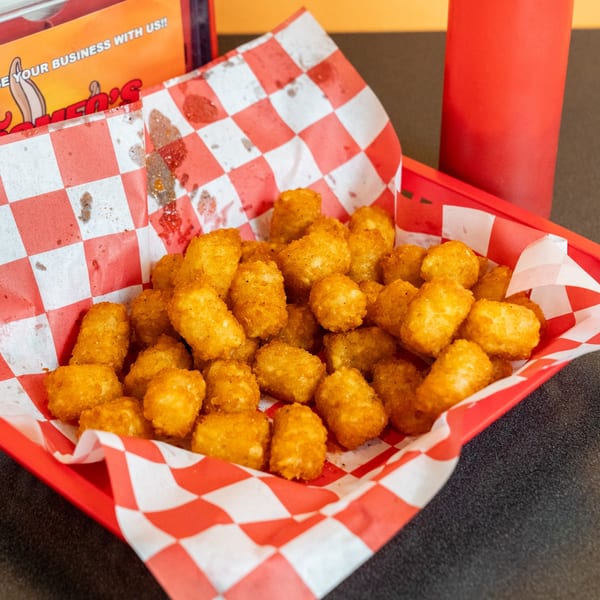A red basket filled with crispy golden tater tots on a red and white checkered paper liner.