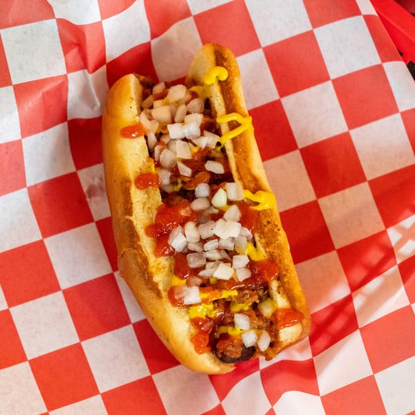 A vegan chili dog with mustard, ketchup, and diced onions on red and white checkered paper.