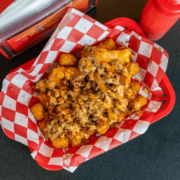 A red basket of vegan tater tots topped with melted cheese, vegan meat, and onions.