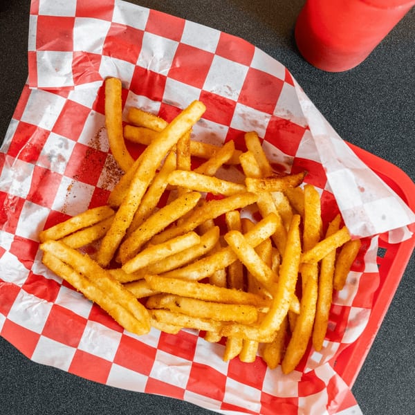 Seasoned vegan french fries in a red plastic basket lined with red and white checkered paper.