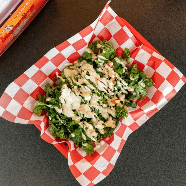 A vegan side salad with green lettuce and creamy dressing in a red and white checkered basket.