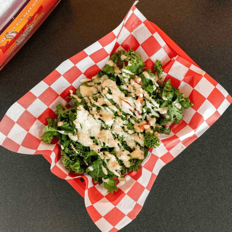 A vegan side salad with green lettuce and creamy dressing in a red and white checkered basket.