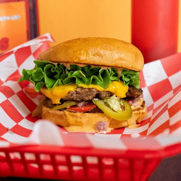 A Romeo's Vegan Burger with lettuce, cheese, tomatoes, and jalapeños in a red checkered basket.