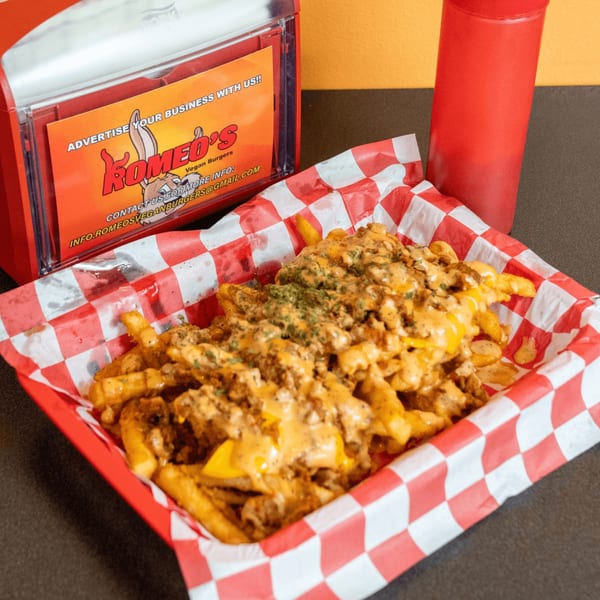 Romeo's Vegan Burgers' loaded fries with cheese sauce and toppings in a red checkered basket.