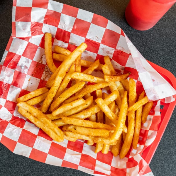 A red plastic basket filled with seasoned vegan french fries on red and white checkered paper.