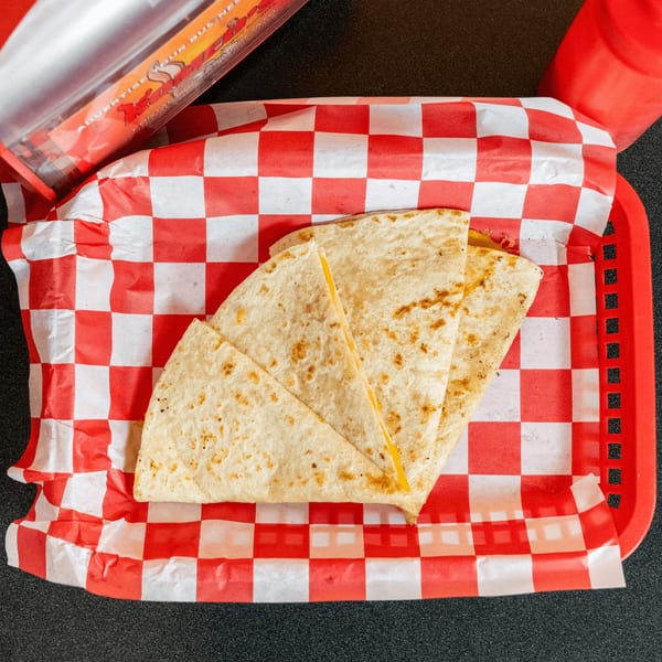Vegan quesadilla slices with melted cheese in a red and white checkered basket.